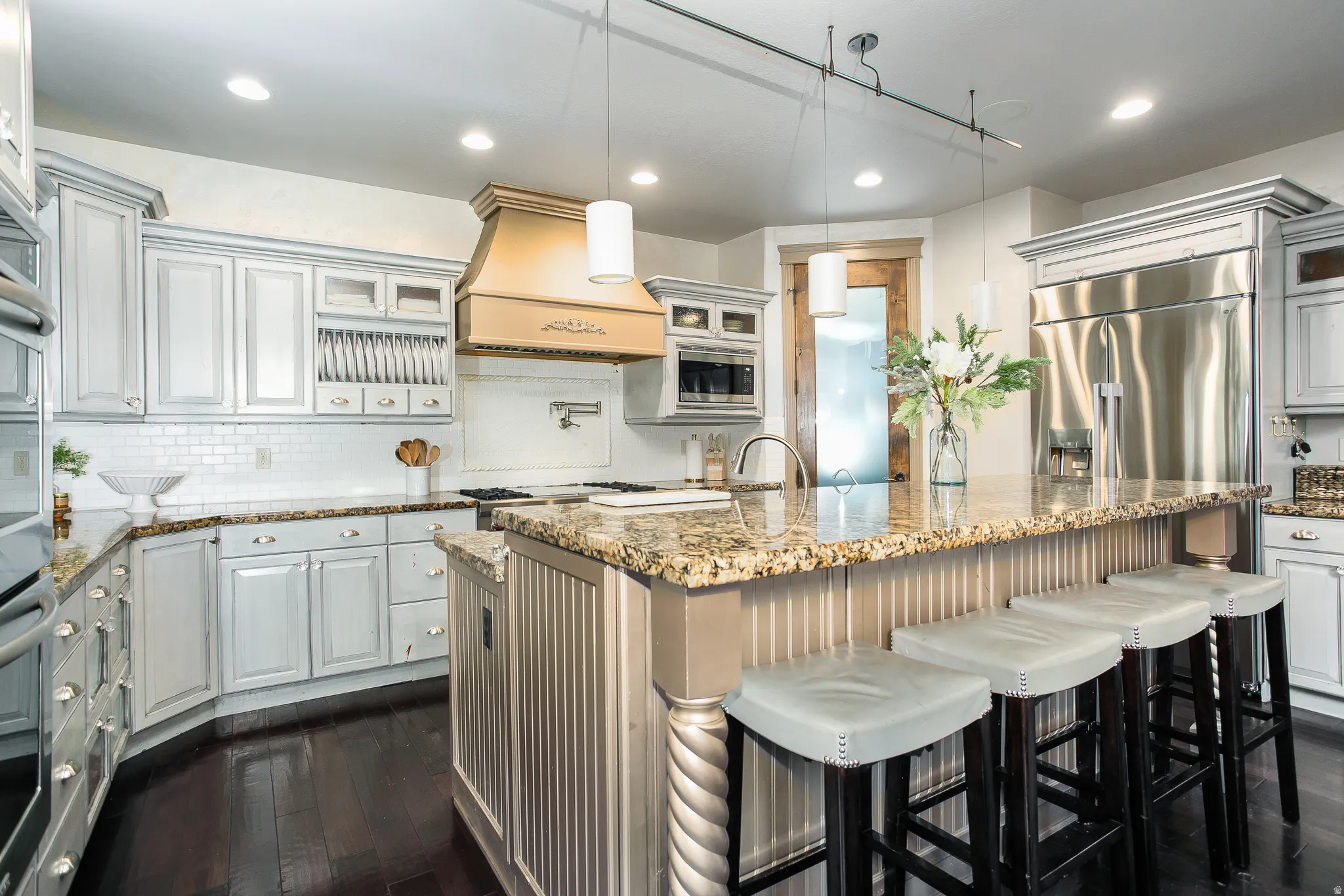 Kitchen featuring an island with a built-in breakfast bar, granite countertops, stainless steel appliances, and distressed white cabinetry