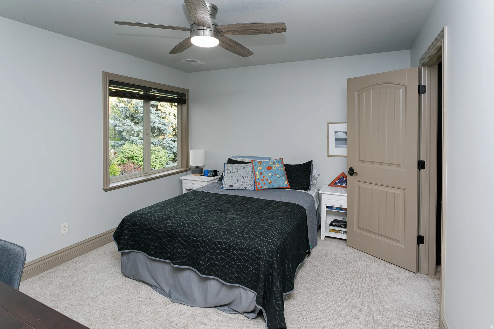 Neutral-toned room featuring a window with exterior foliage, light gray walls, and a ceiling fan with integrated lighting