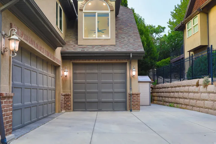 Two-car garage with panel-style doors, brick detailing, and exterior sconce lighting