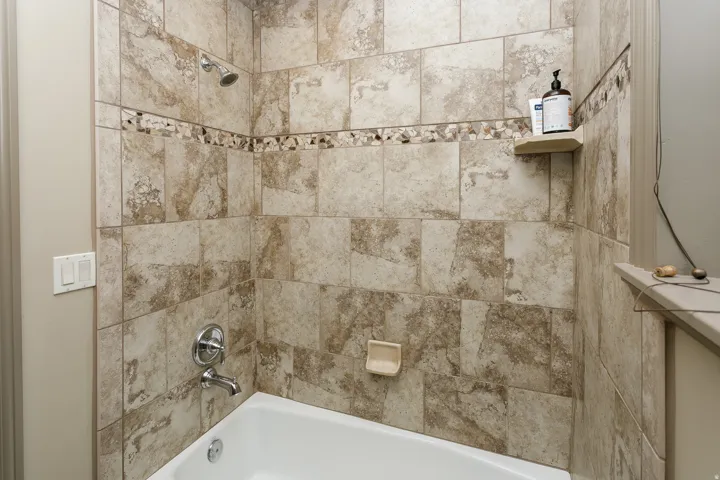 Bathtub and shower combination featuring neutral-toned tile surround with decorative mosaic accent band