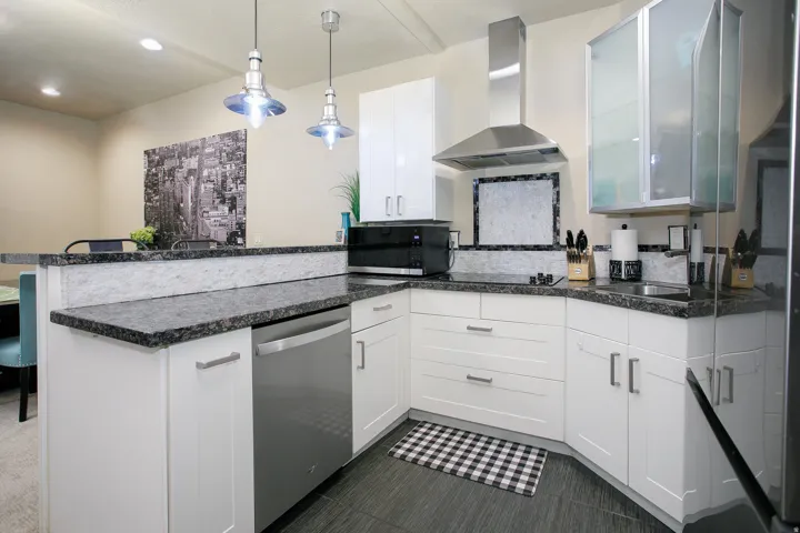 Modern kitchen featuring white cabinetry, dark granite-style countertops, stainless steel appliances, and sleek pendant lighting