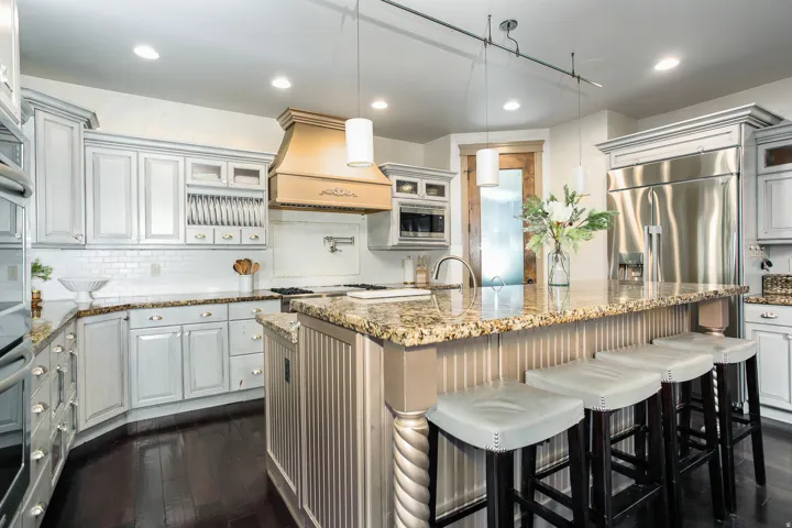 Kitchen featuring an island with a built-in breakfast bar, granite countertops, stainless steel appliances, and distressed white cabinetry