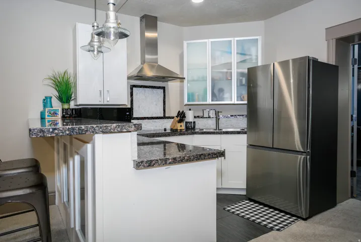 Kitchen featuring granite countertops, white cabinetry, stainless steel appliances, a stainless steel range hood, and pendant lighting