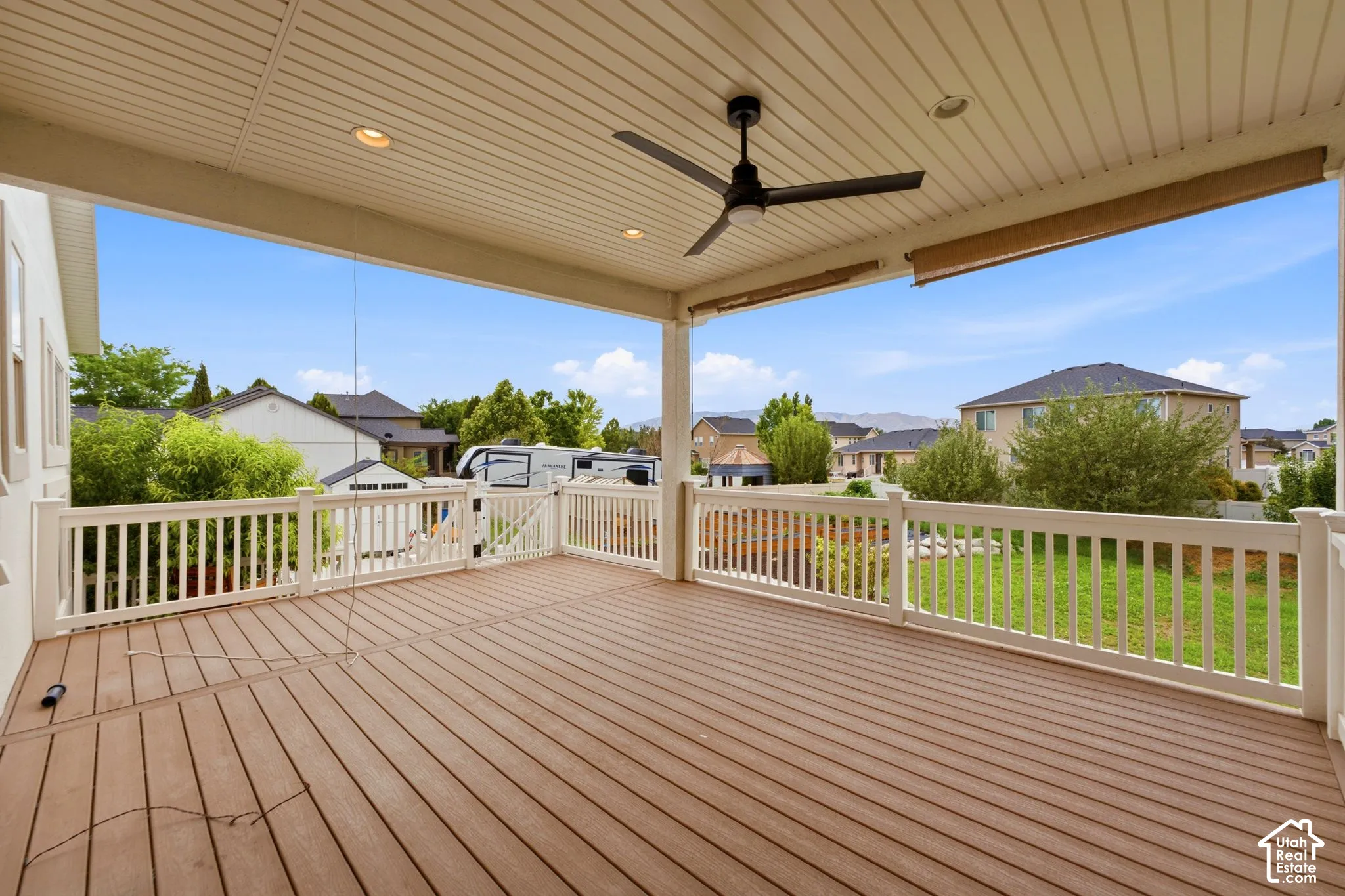 Expansive covered deck featuring composite wood-finish decking, white railing, recessed lighting, and a ceiling fan