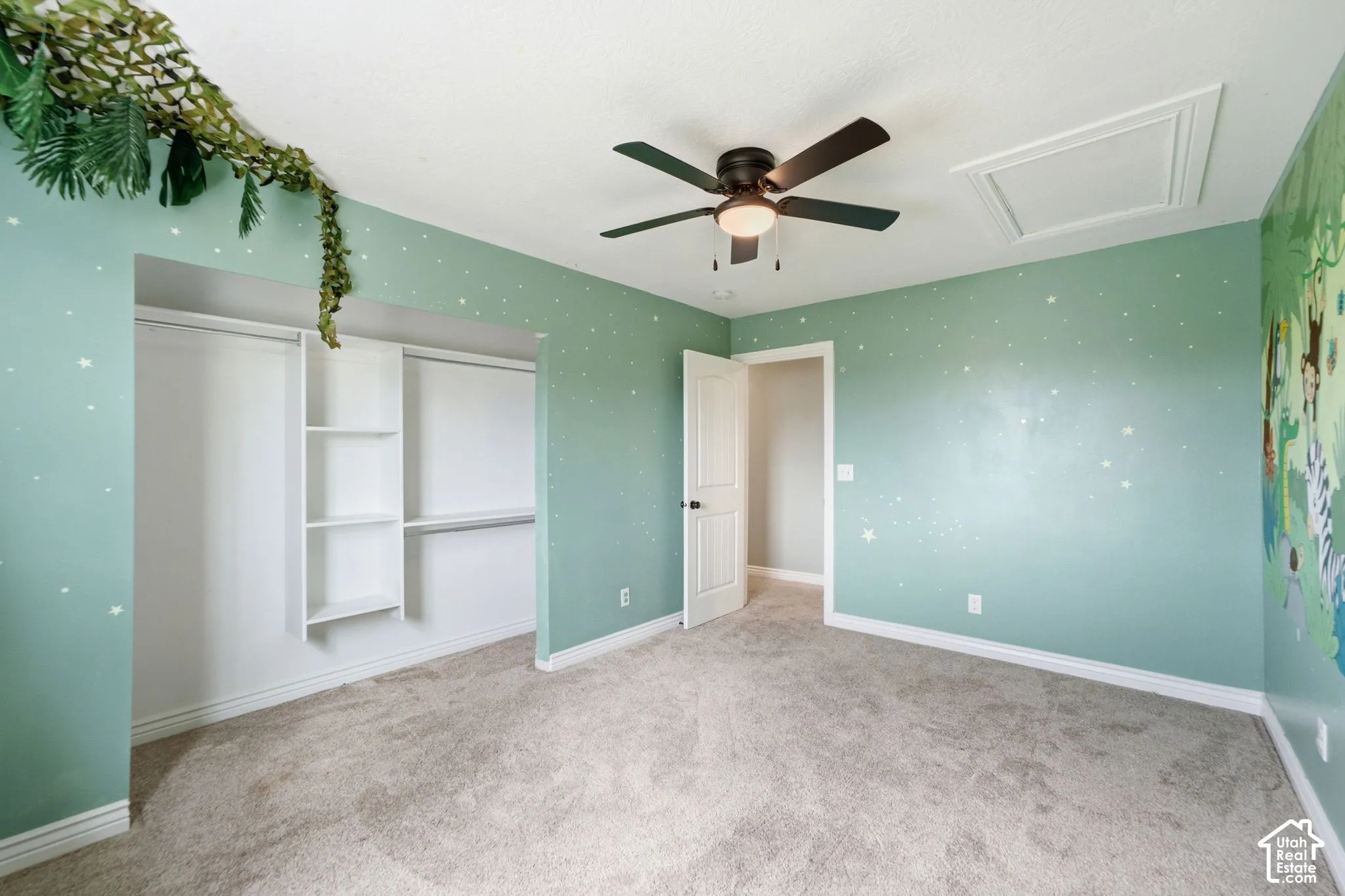 Spacious interior room featuring plush carpet flooring, a built-in closet with shelving and hanging rods, a ceiling fan with integrated lighting, and a white interior door with dark hardware