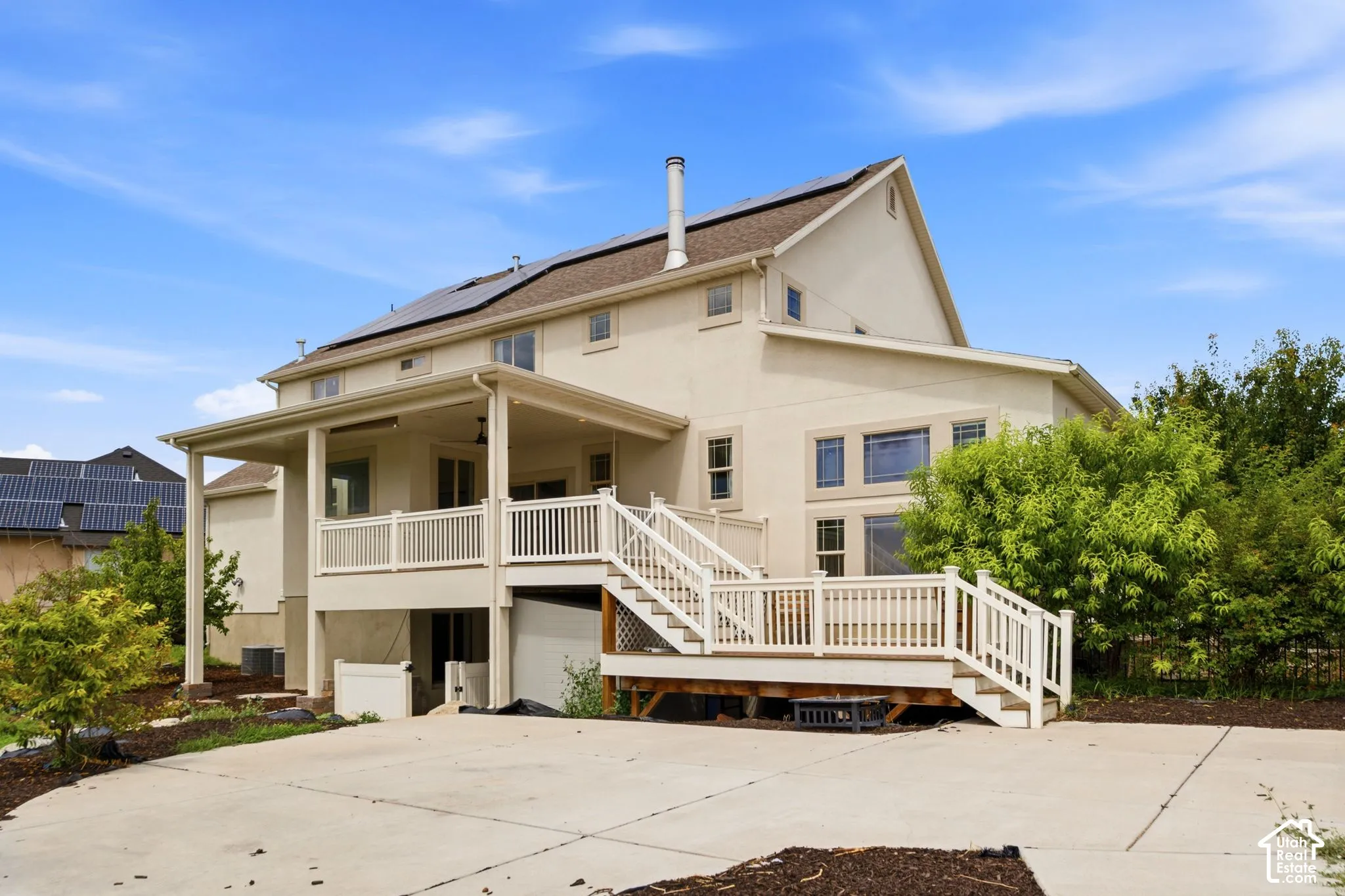 Rear exterior featuring a multi-level deck with white railings, a covered patio, and solar panels on the roof