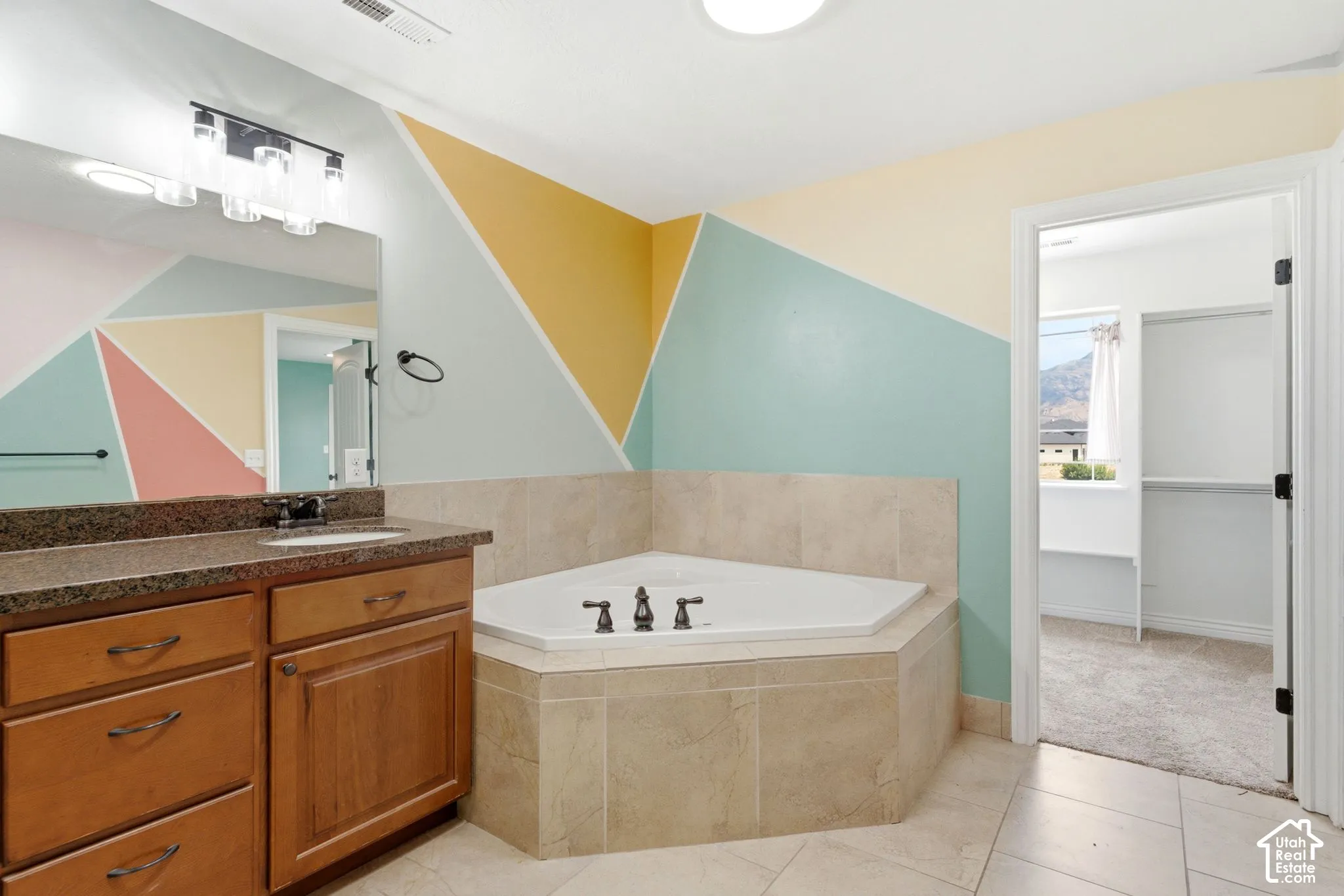 Bathroom featuring an integral corner tub, a single vanity with a dark countertop and undermount sink, a large wall mirror, and tile flooring