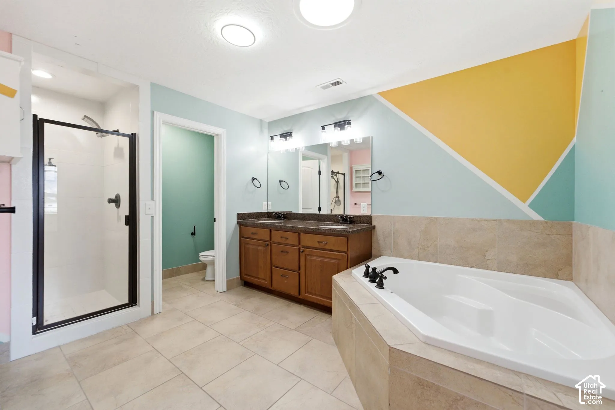 Bathroom featuring a corner soaking tub, a stand-up shower with a frameless glass enclosure, a dual vanity with a dark countertop, and tile flooring