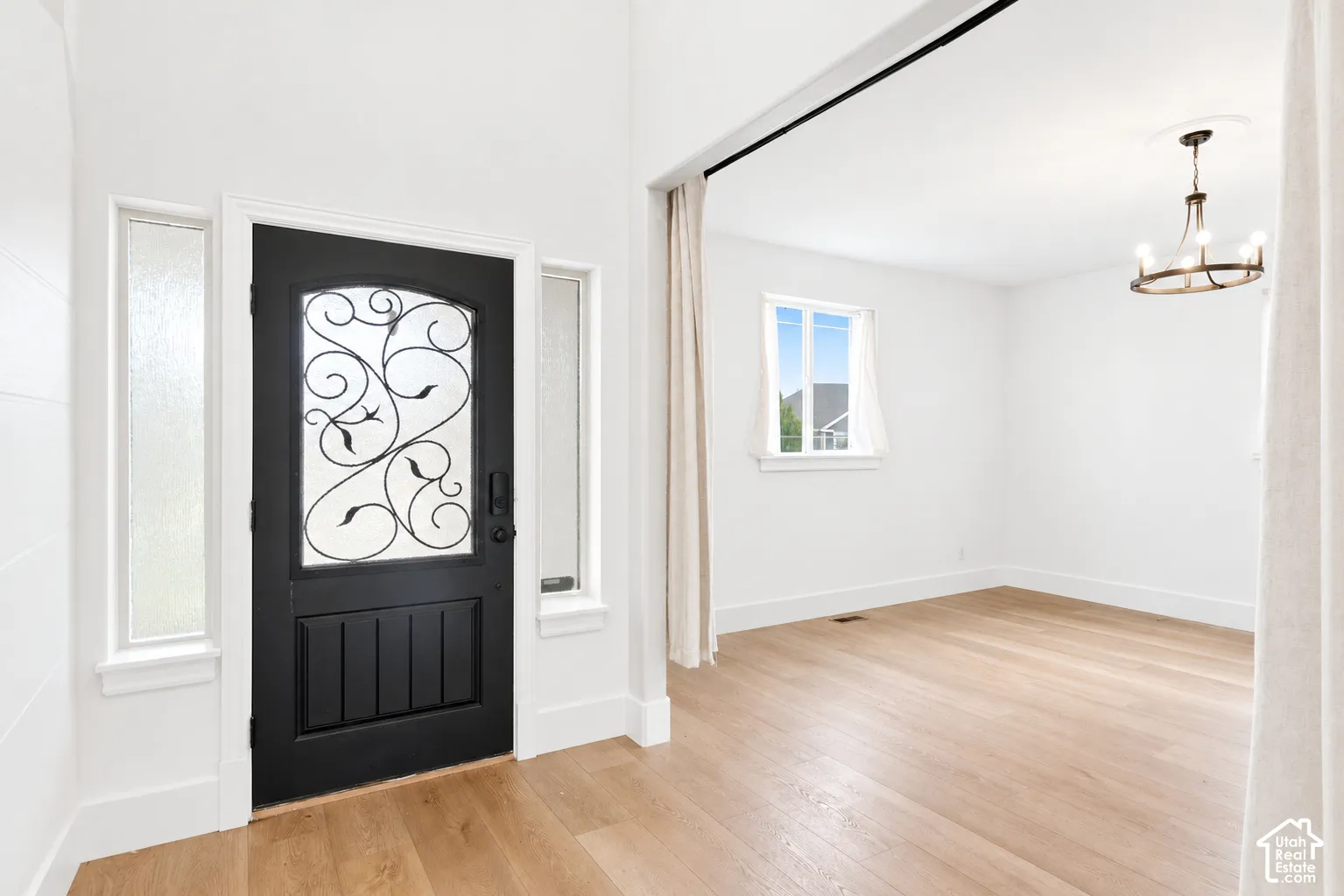Arched entry door with decorative ironwork, frosted glass sidelights, wood-finish flooring, and a contemporary chandelier