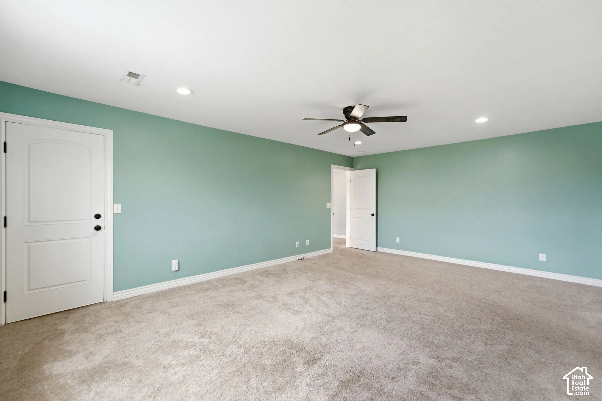 Spacious room featuring light green walls, light-colored carpet flooring, a ceiling fan, and recessed lighting