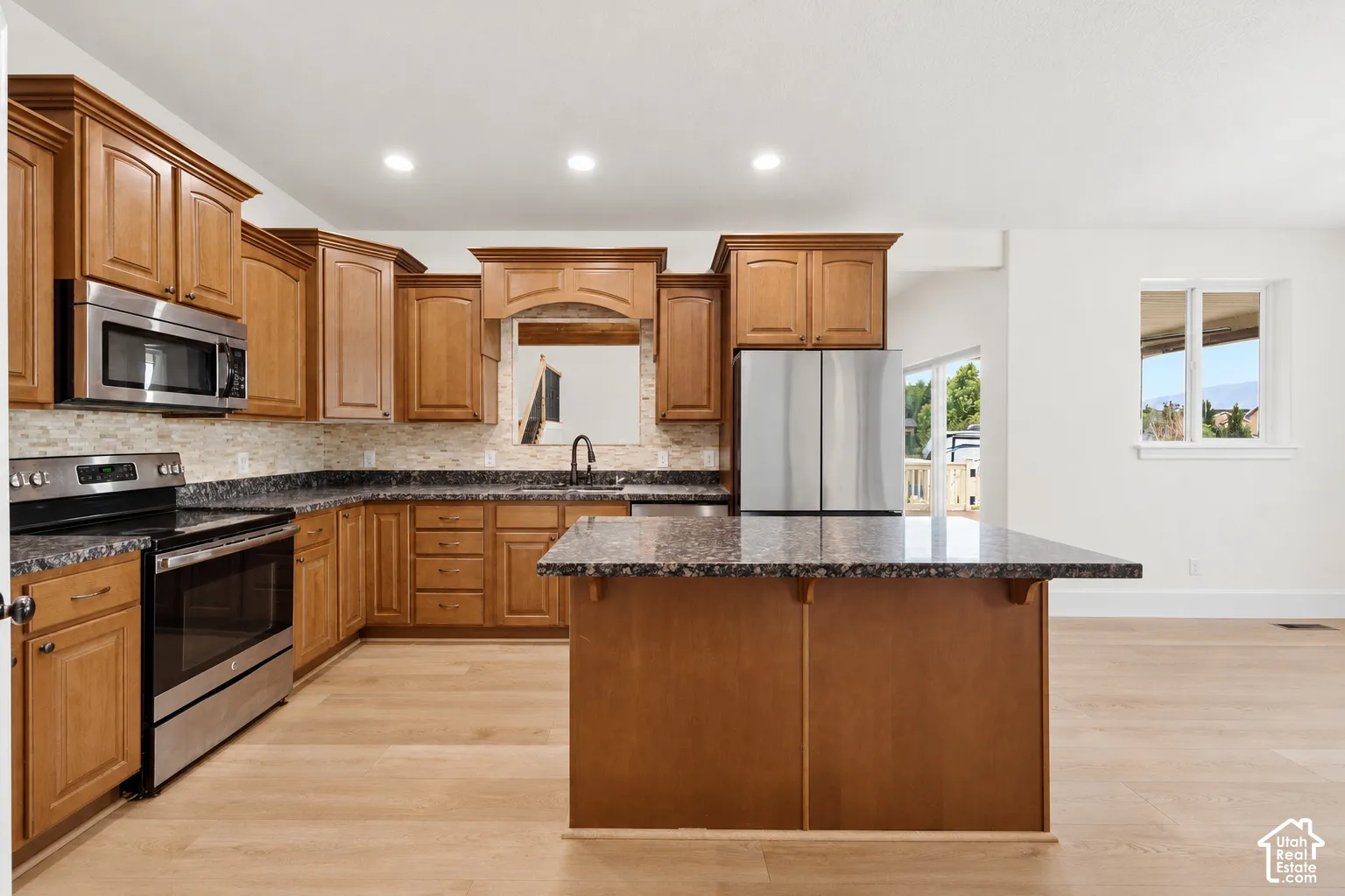 Wood-finish flooring, stainless steel appliances, dark stone countertops, natural wood cabinetry, and a stone-tiled backsplash