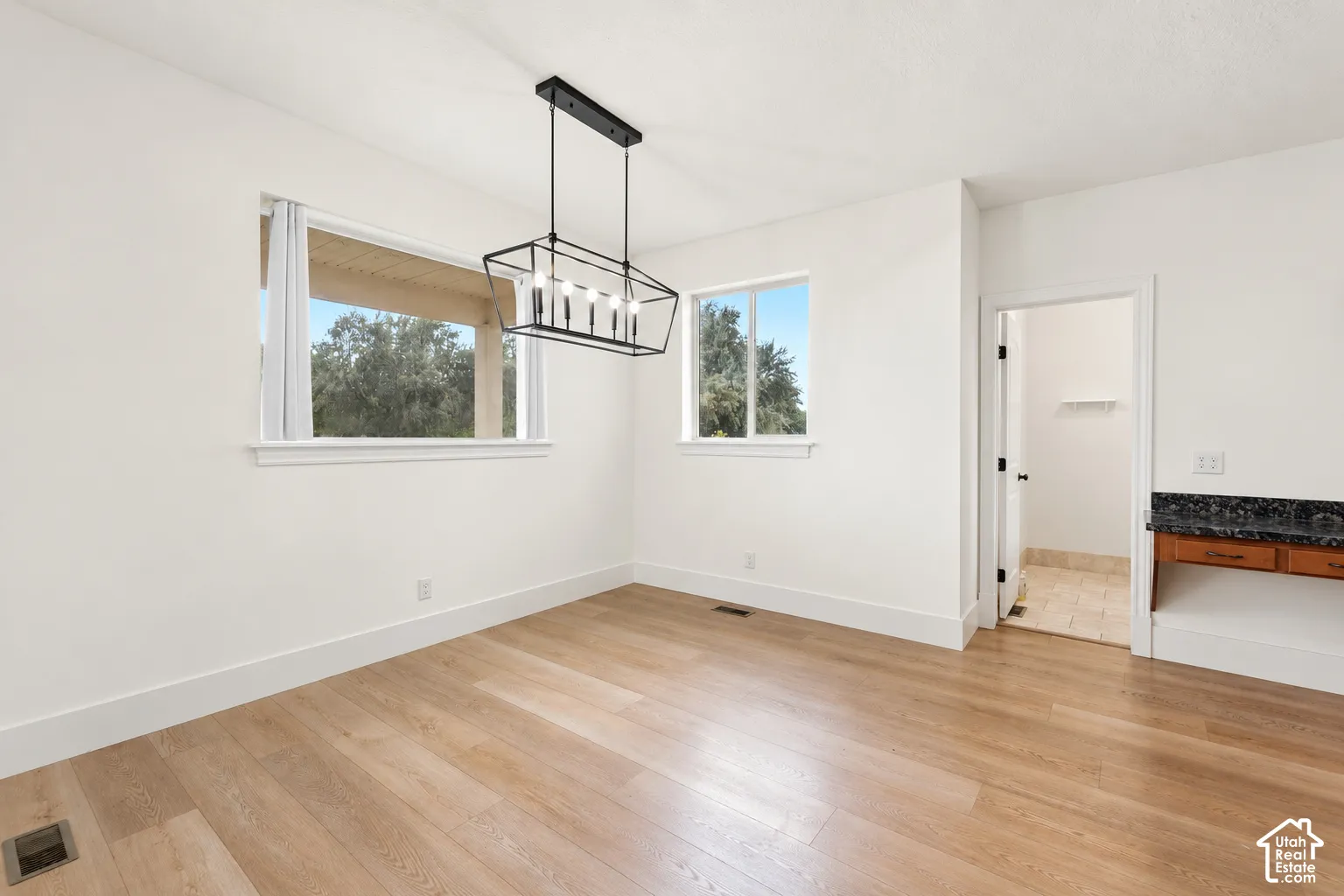Light wood-finish flooring, two large windows, and a modern linear chandelier with a dark finish