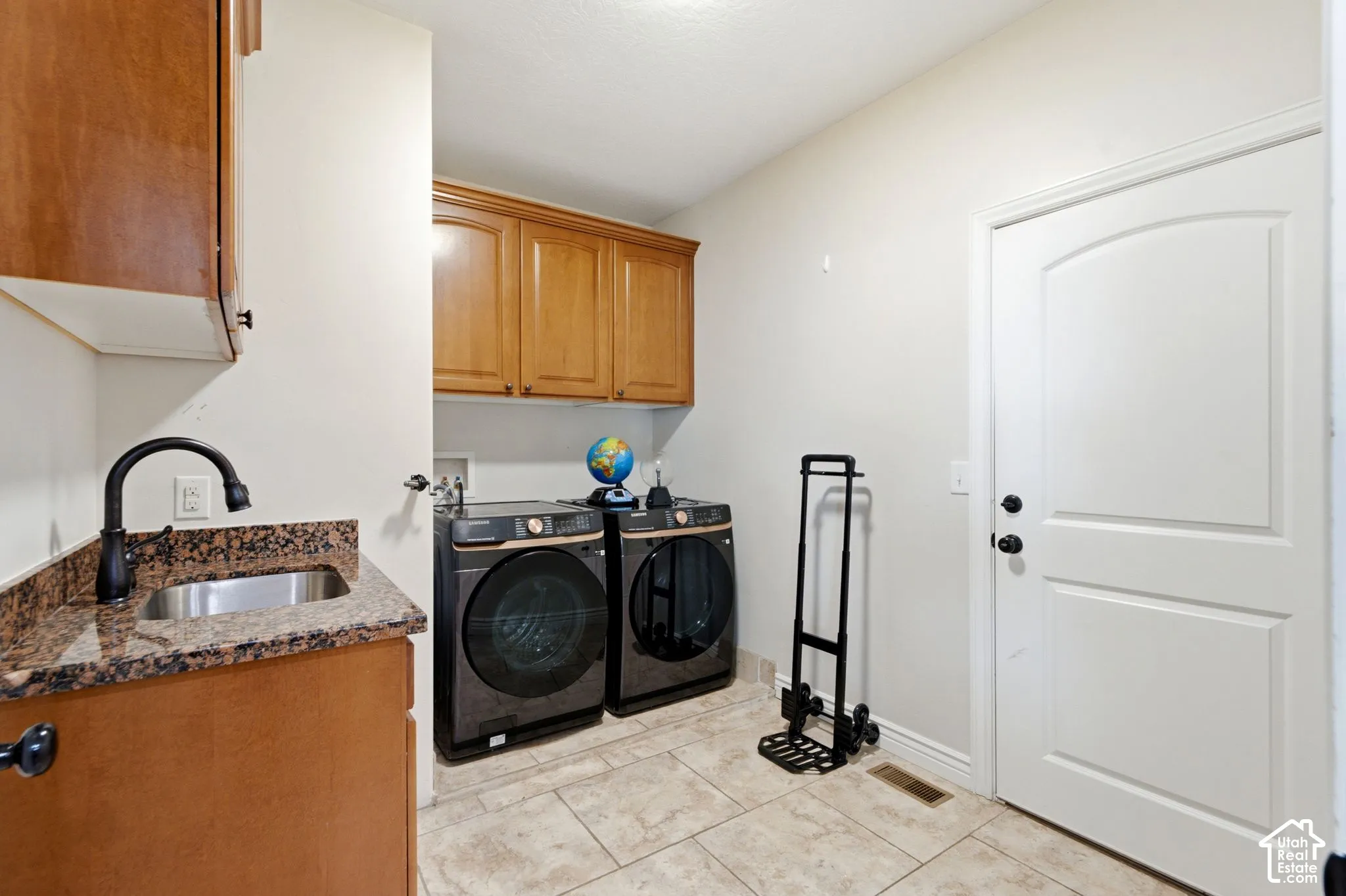 Dedicated laundry room with tile flooring, featuring abundant cabinetry, a utility sink with a dark-finish faucet, and a white arched panel door