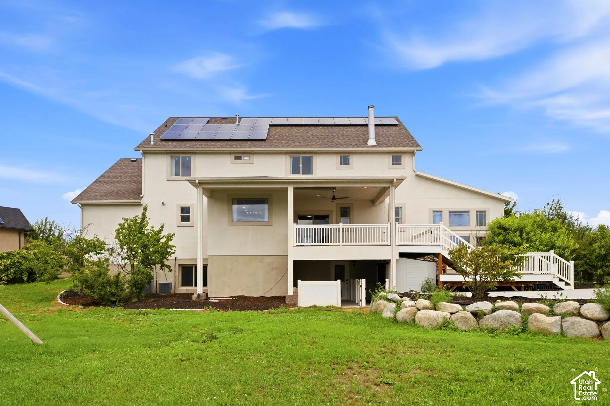 Expansive rear facade featuring a covered patio, multi-level composite decking, and a stone retaining wall