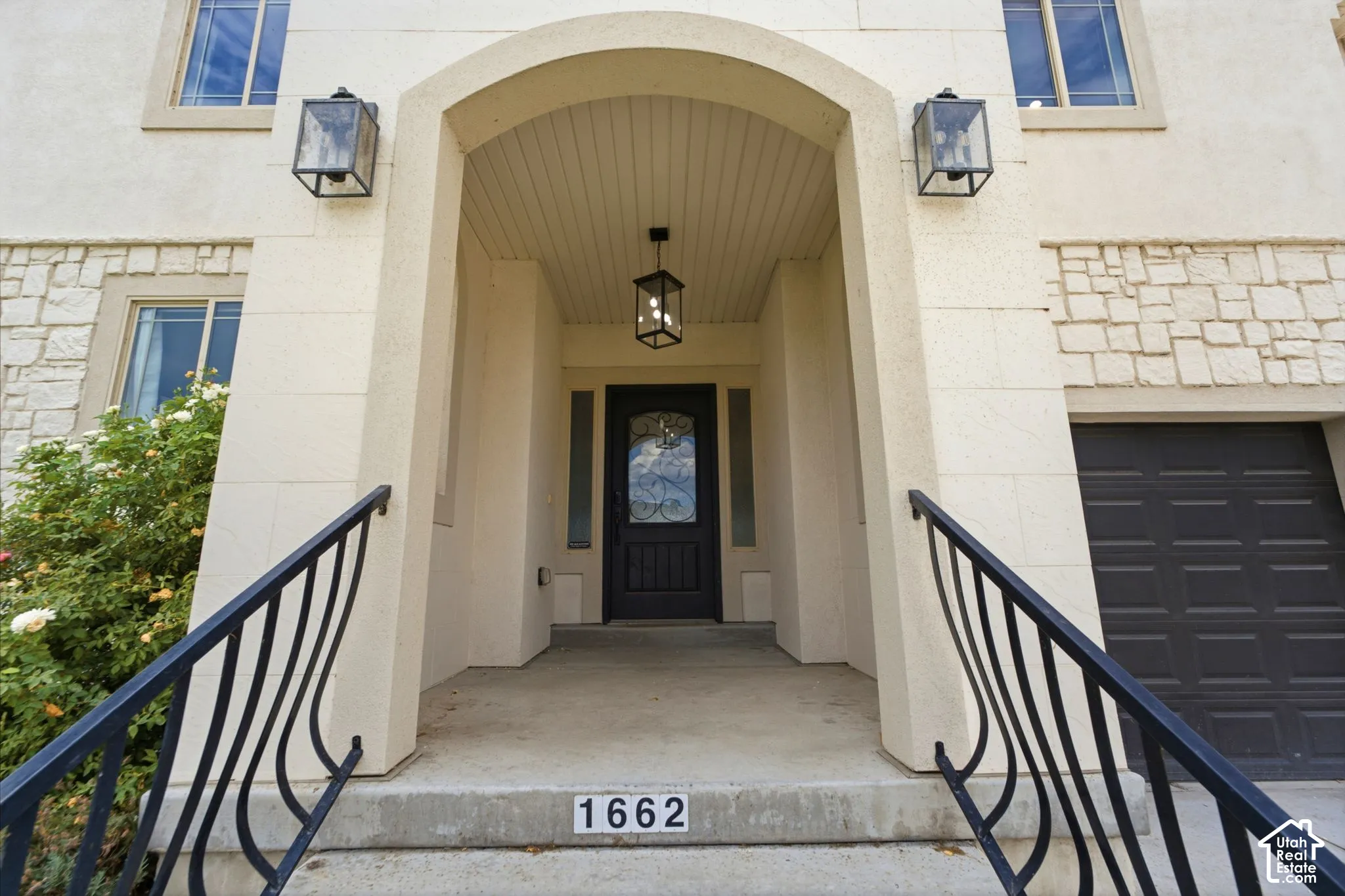 Arched entryway featuring a dark paneled door with decorative glass, flanked by two wall-mounted lanterns
