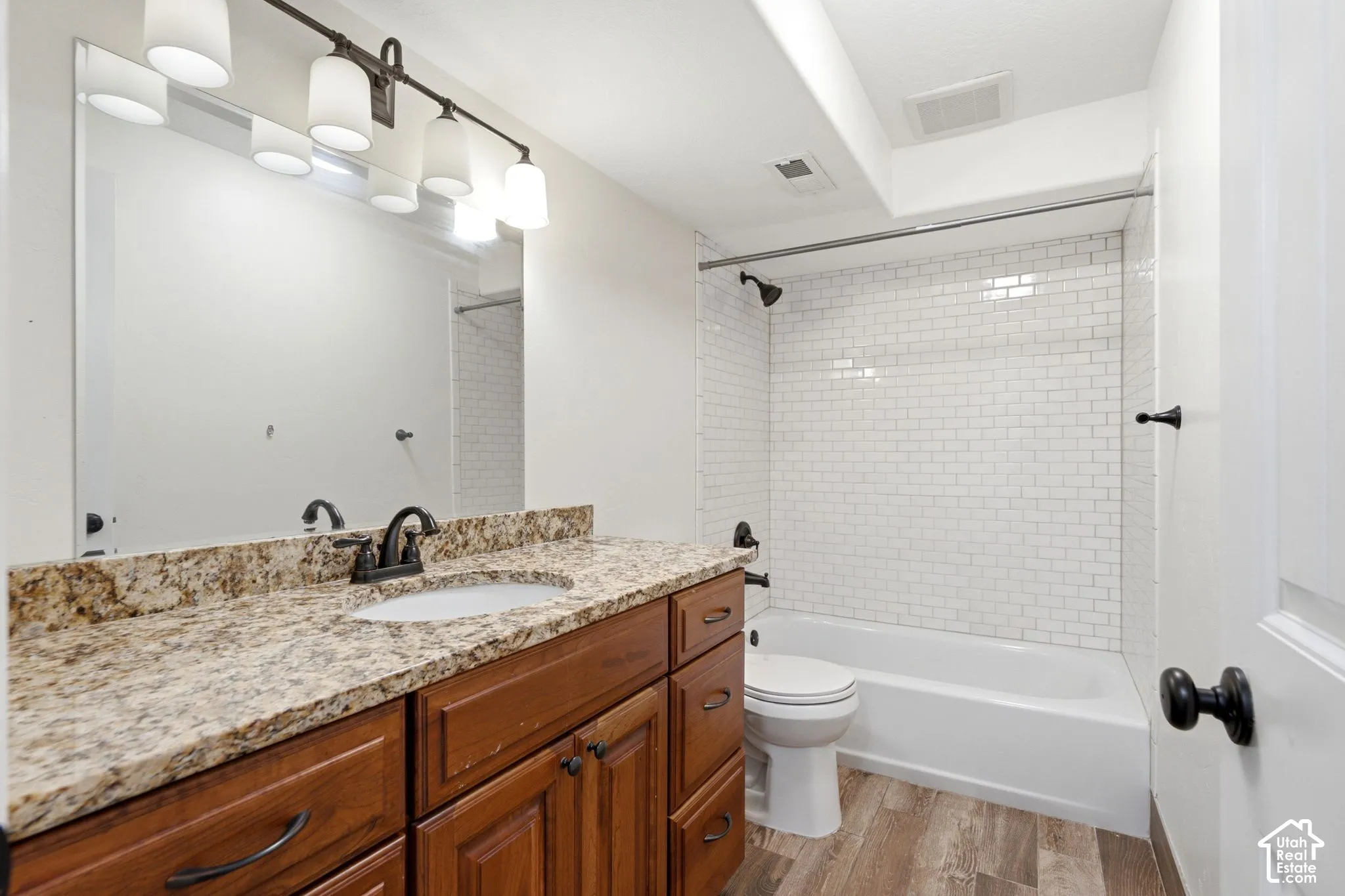 Full bathroom featuring a wood-finish vanity with a granite countertop, undermount sink, and a framed mirror