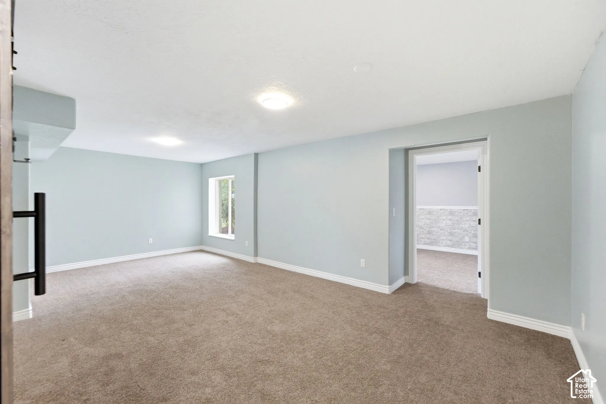 Expansive carpeted room featuring light blue walls, white trim, and a window