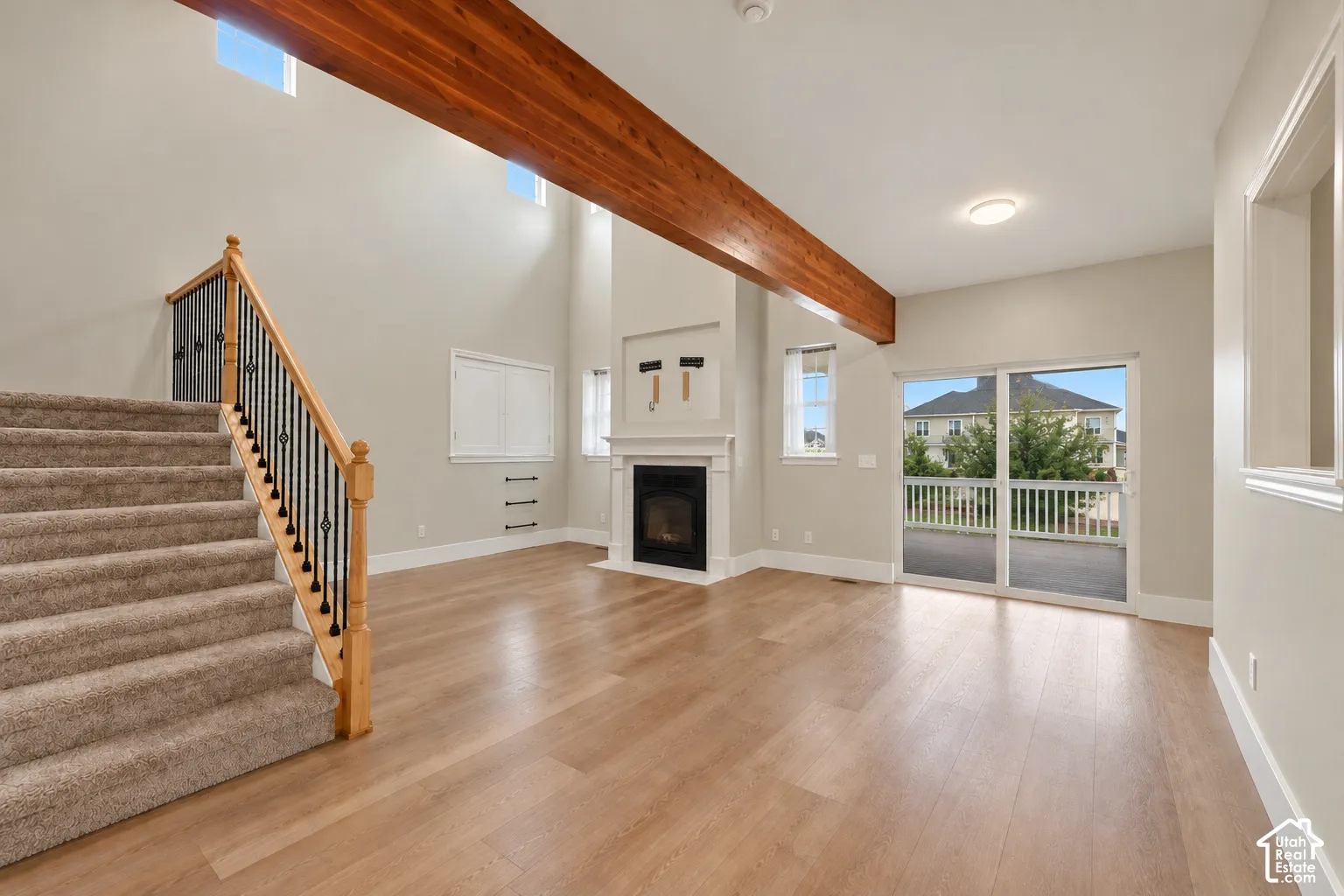 Vaulted ceilings with exposed wood beam, fireplace with mantle, wood-finish flooring, sliding glass door to exterior, and carpeted staircase with wrought iron balusters