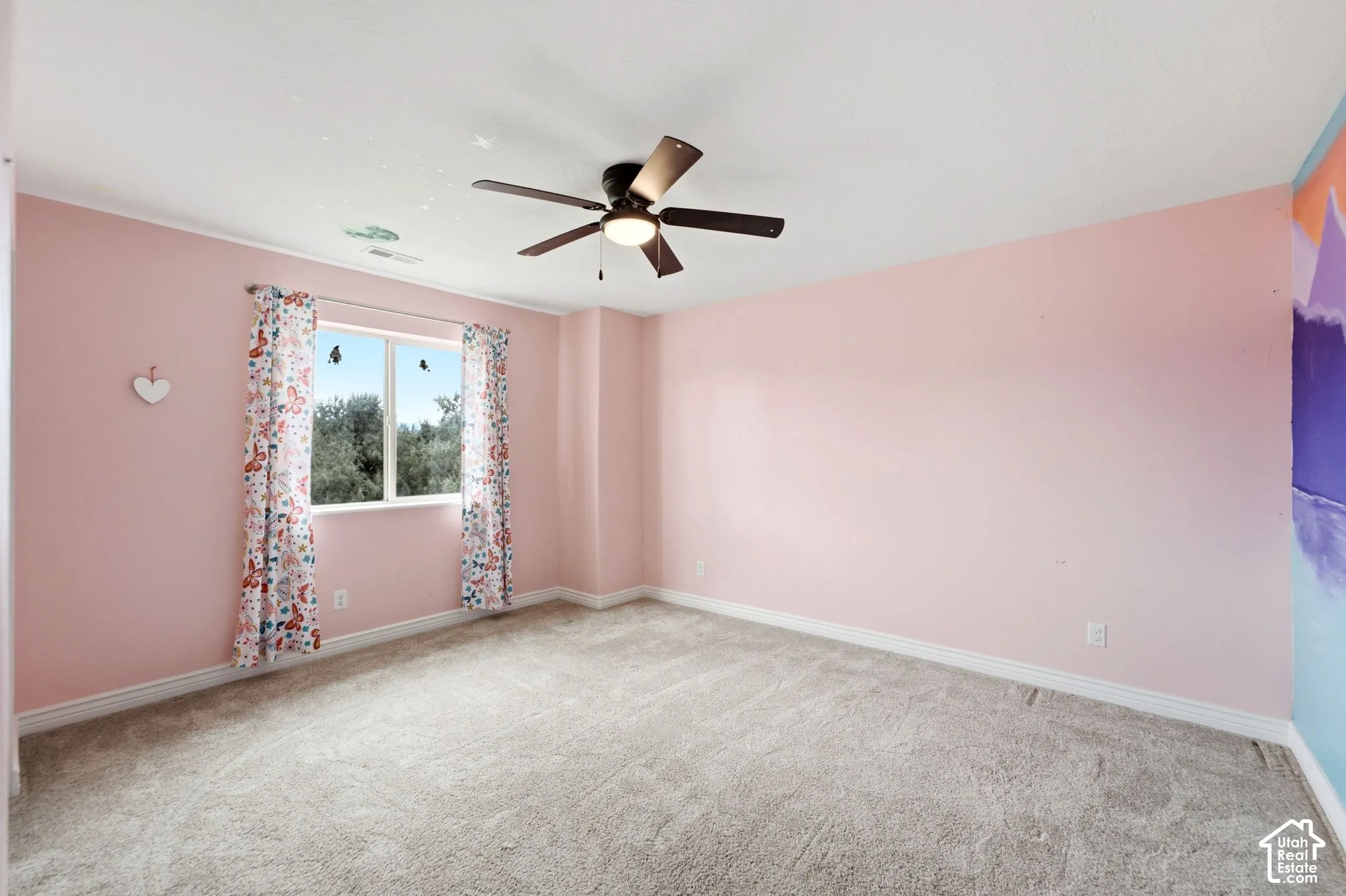 Bedroom featuring light pink walls, gray carpet flooring, a window with exterior tree views, white baseboards, and a ceiling fan with integrated lighting