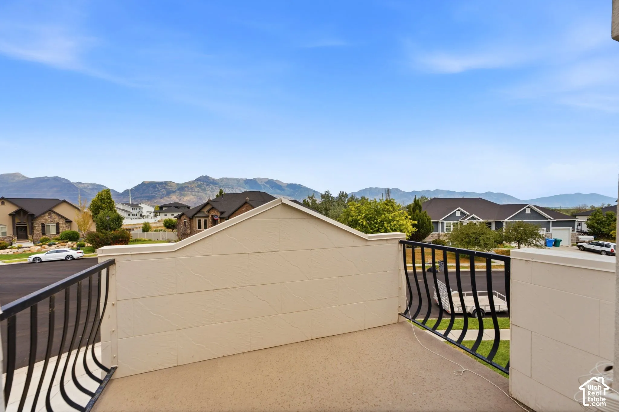 Outdoor balcony featuring black wrought iron railings, a textured beige parapet wall, and a concrete-finish surface