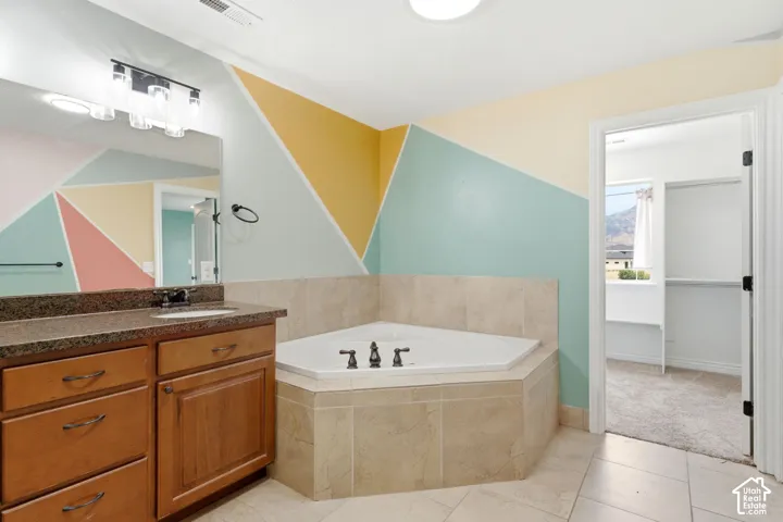 Bathroom featuring an integral corner tub, a single vanity with a dark countertop and undermount sink, a large wall mirror, and tile flooring