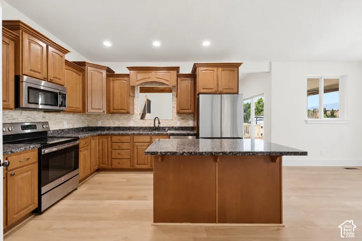 Wood-finish flooring, stainless steel appliances, dark stone countertops, natural wood cabinetry, and a stone-tiled backsplash