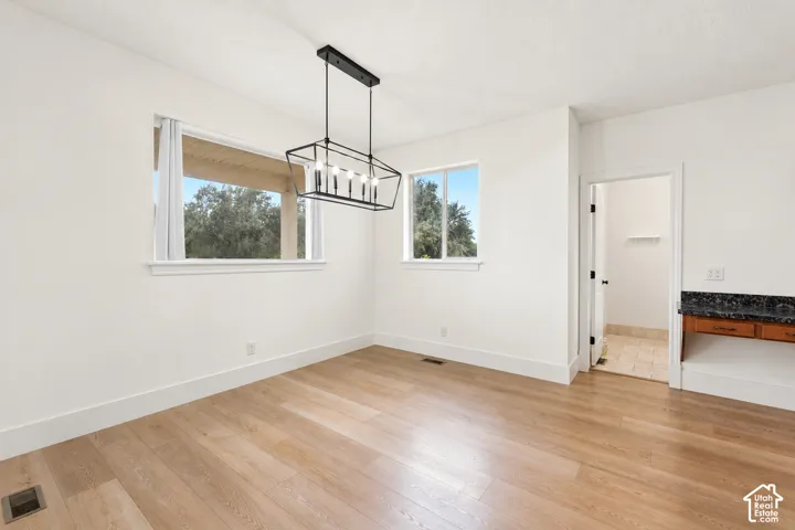 Light wood-finish flooring, two large windows, and a modern linear chandelier with a dark finish