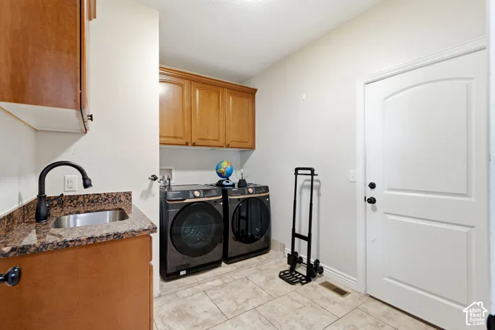 Dedicated laundry room with tile flooring, featuring abundant cabinetry, a utility sink with a dark-finish faucet, and a white arched panel door