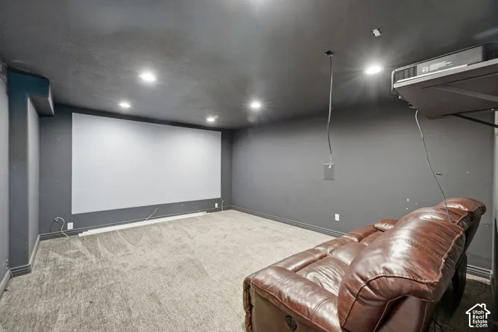 Dedicated media room featuring a large projection screen, dark painted walls, recessed ceiling lighting, and textured carpeting