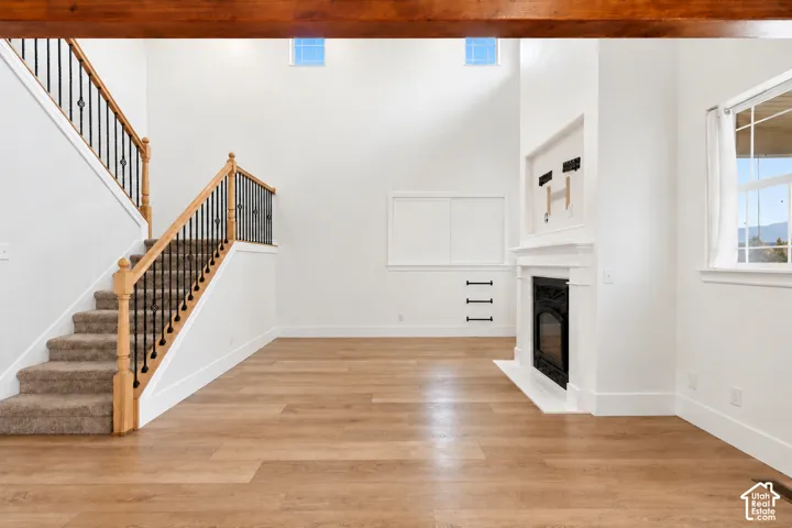 Two-story living area with wood-finish flooring, a white-mantled fireplace, and a carpeted staircase with wrought iron balusters