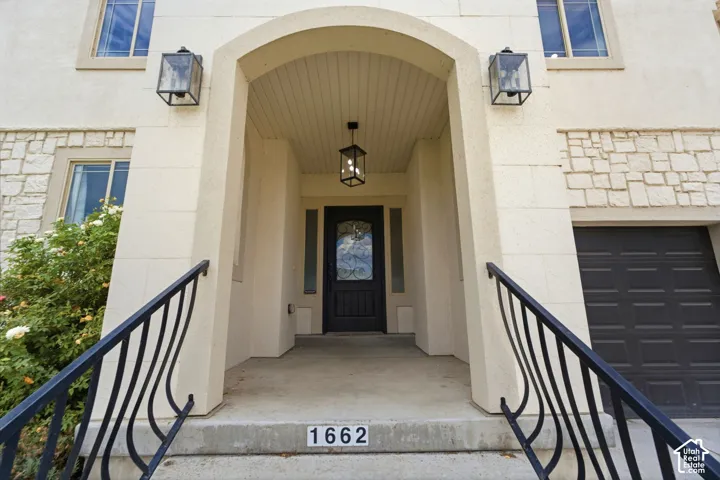 Arched entryway featuring a dark paneled door with decorative glass, flanked by two wall-mounted lanterns