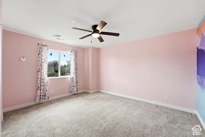Bedroom featuring light pink walls, gray carpet flooring, a window with exterior tree views, white baseboards, and a ceiling fan with integrated lighting