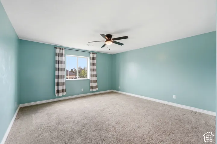 Spacious room featuring light blue walls, gray carpet, a ceiling fan, and a large window
