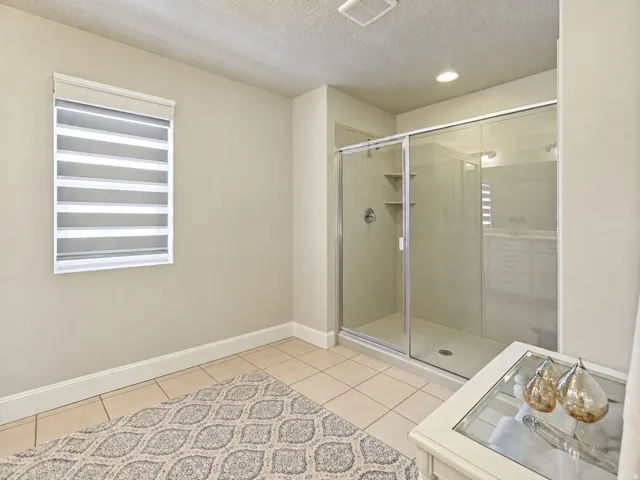 Glass-enclosed shower with built-in shelving, recessed lighting, and tile flooring