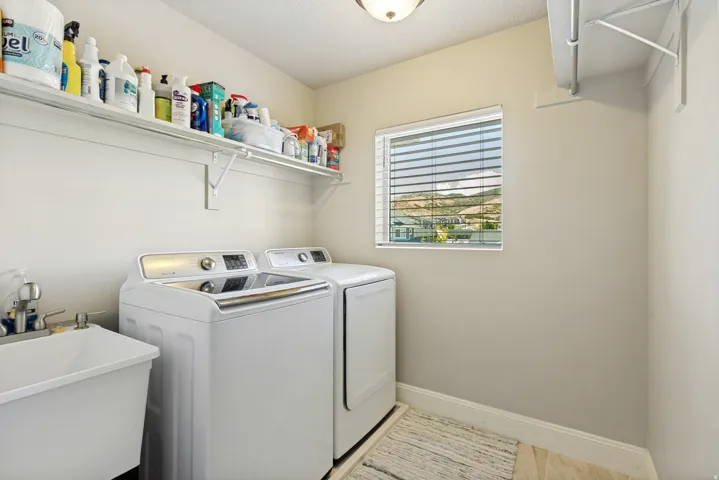 Dedicated laundry area featuring a utility sink with dual faucets, built-in shelving, a window with blinds, and tile flooring