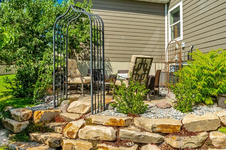 Outdoor patio area featuring a decorative metal arbor, a stone retaining wall, and verdant landscaping