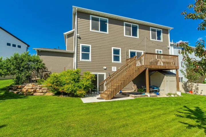 Rear exterior featuring horizontal siding, a multi-level wood deck, a patio, stone landscaping, and a spacious lawn
