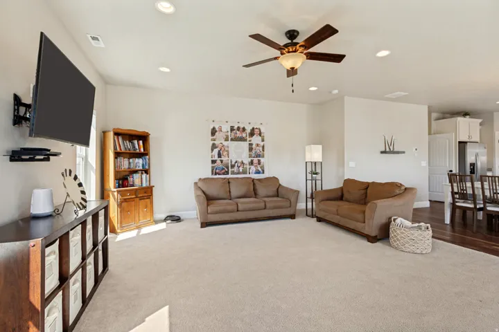 Open-concept living area featuring a ceiling fan with integrated lighting, recessed ceiling lights, and light-colored carpeting