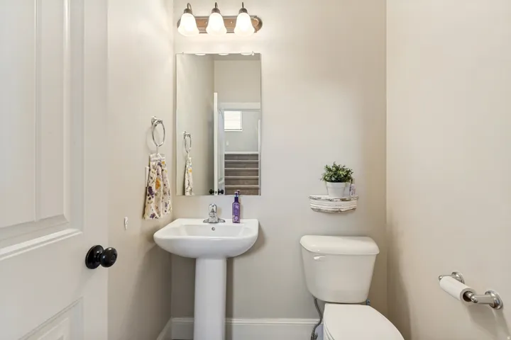 Pedestal sink with chrome faucet, wall-mounted mirror, and three-light vanity fixture