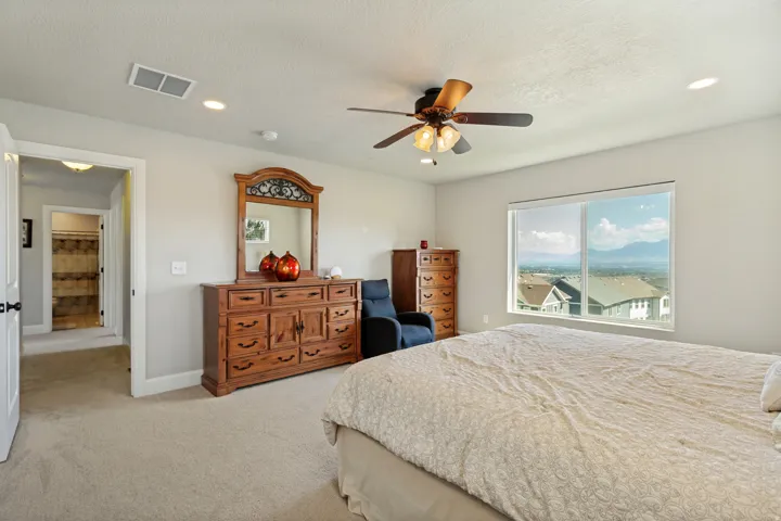 Expansive bedroom featuring neutral carpeting, a large picture window, and a ceiling fan with integrated lighting
