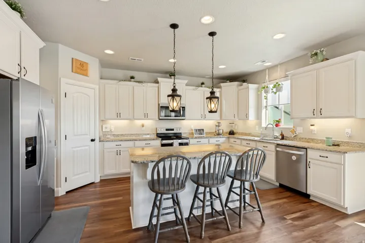 Kitchen featuring white cabinetry, granite countertops, stainless steel appliances, and a central island with pendant lighting