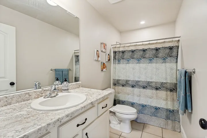 Bathroom featuring a vanity with a light-toned countertop and an integrated sink, white cabinetry with dark hardware, a spacious wall mirror, and a bathtub & shower area