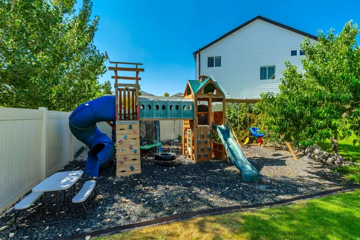 Expansive backyard featuring a multi-level wooden playset with a tube slide, rock climbing wall, and swing set