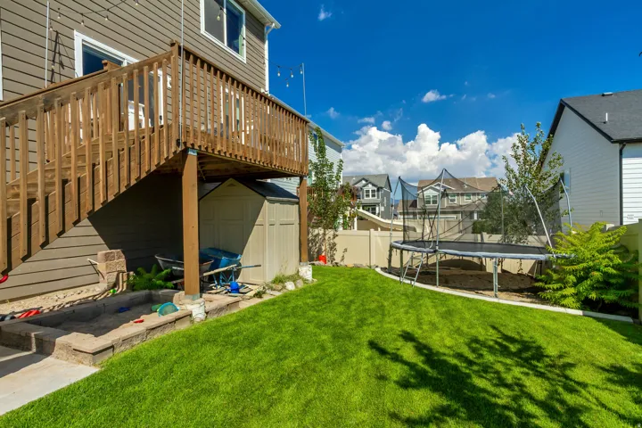 Expansive backyard featuring a lush lawn, a multi-level wood deck, a built-in sandbox with retaining wall, and a storage shed under the deck