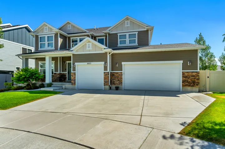 Two-story residence featuring a covered front porch with white columns, a large concrete driveway, two attached garages, a stone facade accent, and dormer windows