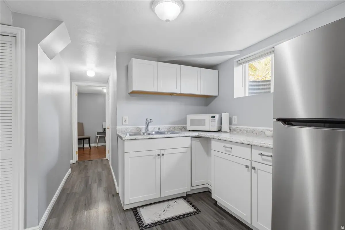 Compact kitchen area featuring white cabinetry, a stainless steel refrigerator, and wood-finish flooring