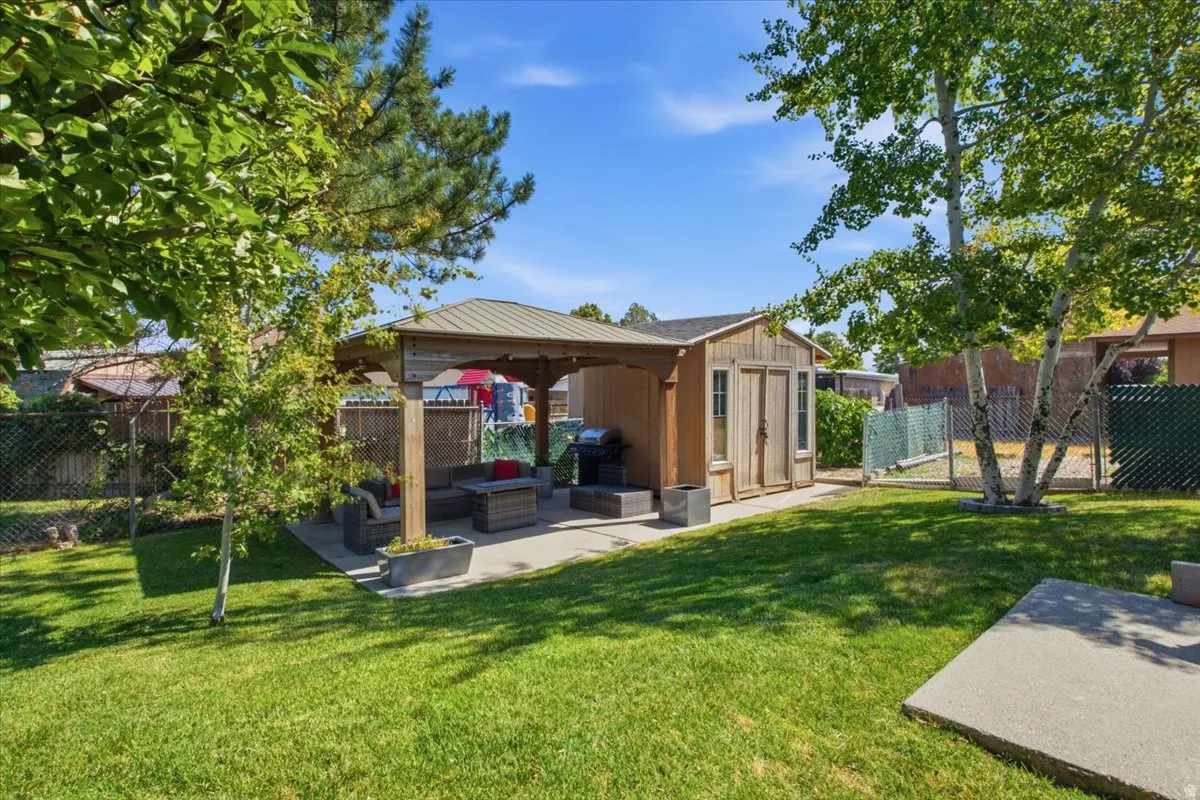 Expansive backyard featuring a central lawn, mature trees, and a concrete patio under a wooden gazebo with a metal roof