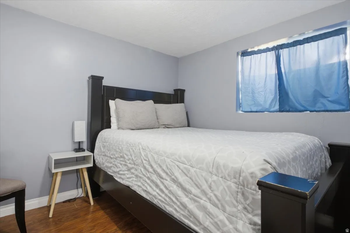 Bedroom featuring light gray wall paint, a window with blue privacy drapes, and wood-finish flooring