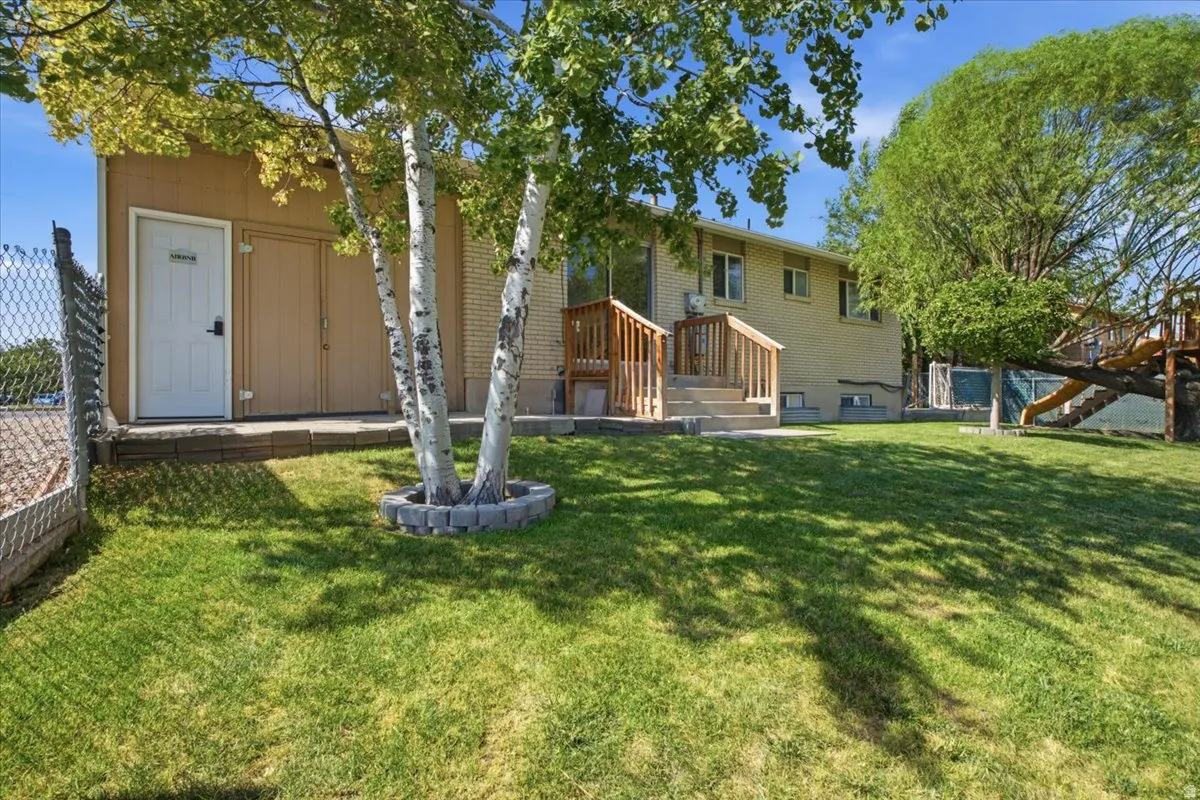 Spacious backyard featuring a lush lawn, mature trees, and a terraced concrete patio