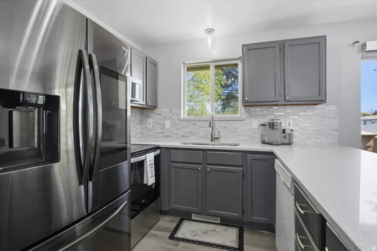 Kitchen featuring stainless steel appliances, gray cabinetry, white countertops, a tiled backsplash, and wood-finish flooring